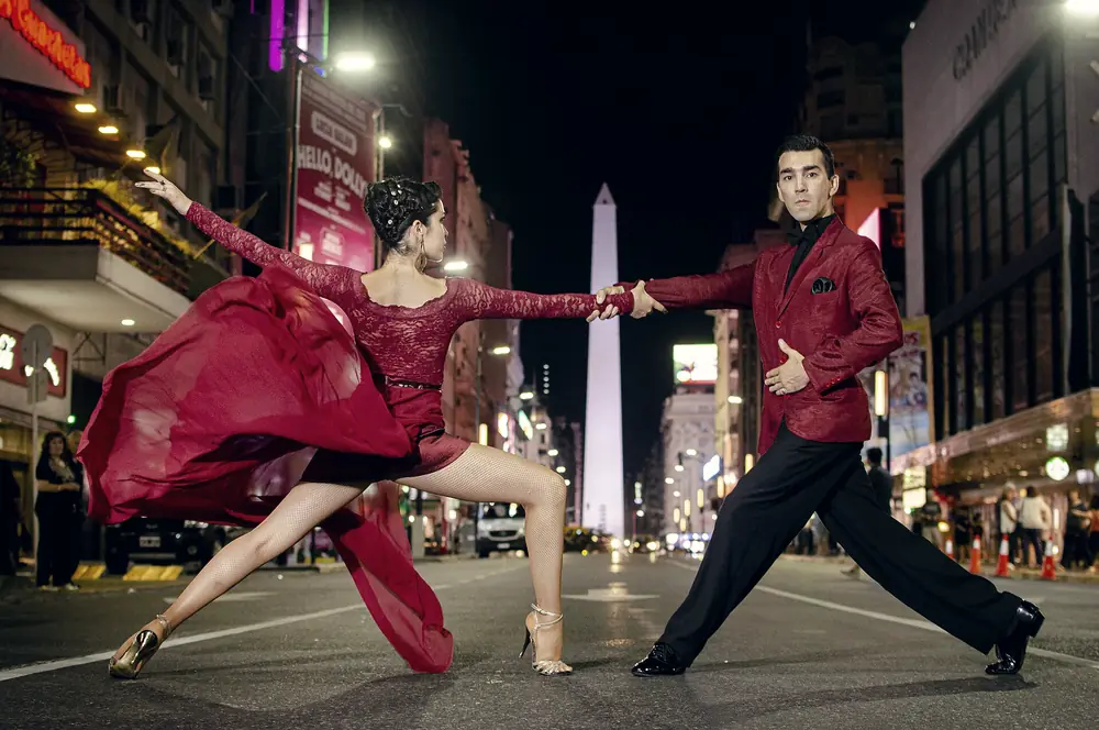 Casal dançando tango na Avenida Corrientes, com o Obelisco ao fundo